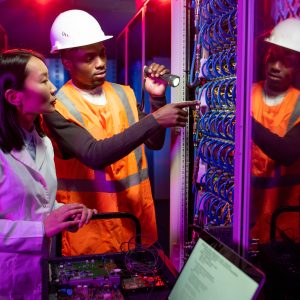 African American workman in hardhat repairing server and explaining reason of server breakdown in data center